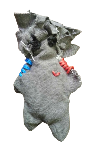 A transparent image of Scranr. Scranr is a dark grey and poorly made ragdoll. He has curly and spiky hair, black eyes (supposed to resemble eyepatches), two horns on each side (barely visible), and he has blue embroidery on one shoulder and red embroidery on the other. He has a small red heart on his chest.